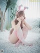 A woman in a pink bunny outfit sitting on a bed of white pebbles.