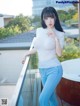 A woman in a white top and blue jeans posing on a balcony.