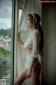 A woman in a white lingerie leaning against a window.