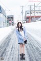 A woman standing in the middle of a snow covered road.