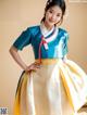 A woman in a blue and yellow hanbok poses for a picture.