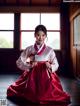 A woman in a red and white hanbok sitting on the floor.