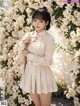 A woman standing in front of a wall of white flowers.