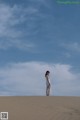 A woman in a white dress standing on top of a sand dune.