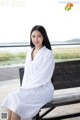 A woman in a white robe sitting on a bench.